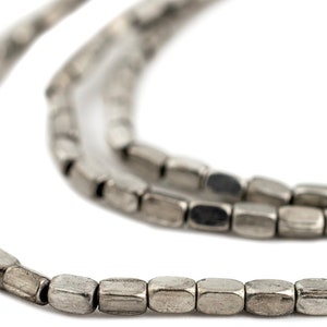 May include: A strand of silver-toned metal beads, each bead is a rectangular shape with a slightly rounded edge. The beads are strung together to form a necklace or bracelet.