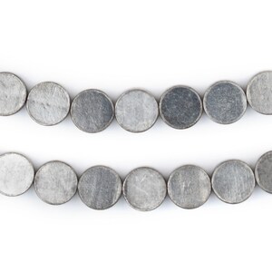 Pu&ograve; includere: Una collana di perline ovali color argento, disposte in due file. Le perline sono lisce e hanno una superficie leggermente ruvida.