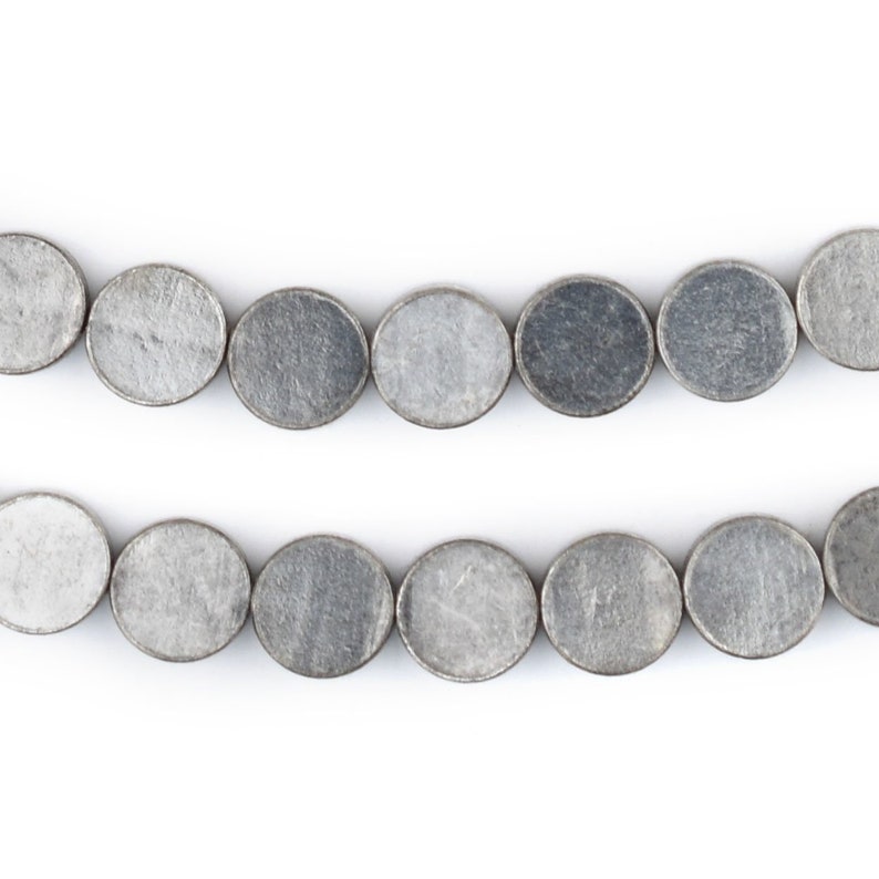 Pu&ograve; includere: Una collana di perline ovali color argento, disposte in due file. Le perline sono lisce e hanno una superficie leggermente ruvida.