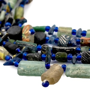 May include: A necklace with a collection of colourful beads. The beads are in shades of blue, green, brown, and clear, with a mix of shapes and sizes. The necklace is strung on a blue cord.
