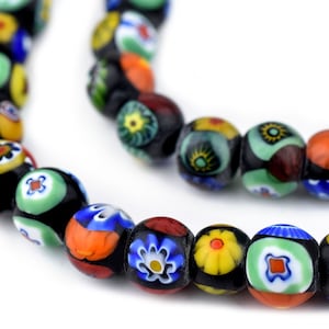 Puede incluir: Primer plano de un collar de cuentas de vidrio millefiori de colores. Las cuentas son redondas, con intrincados diseños florales y geométricos en rojo, azul, amarillo, verde y blanco, sobre un fondo negro. Las cuentas están ensartadas.