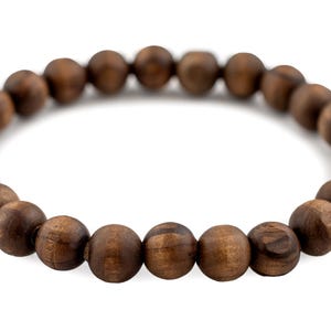 May include: A dark brown wooden bead bracelet. The beads are round and have a natural wood grain appearance. The bracelet is strung on an elastic band, and is displayed against a white background.
