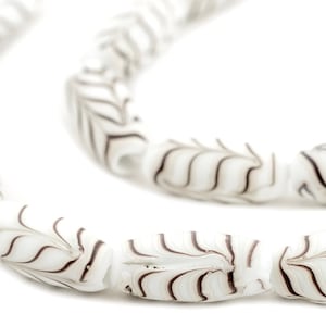 May include: A strand of white glass beads with brown swirl designs. The beads are cylindrical and have a smooth, polished finish.