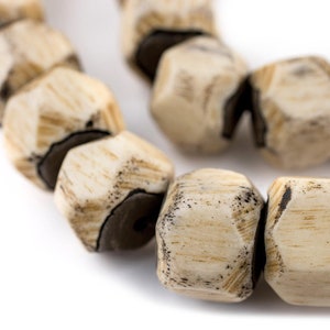 May include: A close-up of a strand of beige and brown wooden beads. The beads are faceted and have a rough, natural texture.