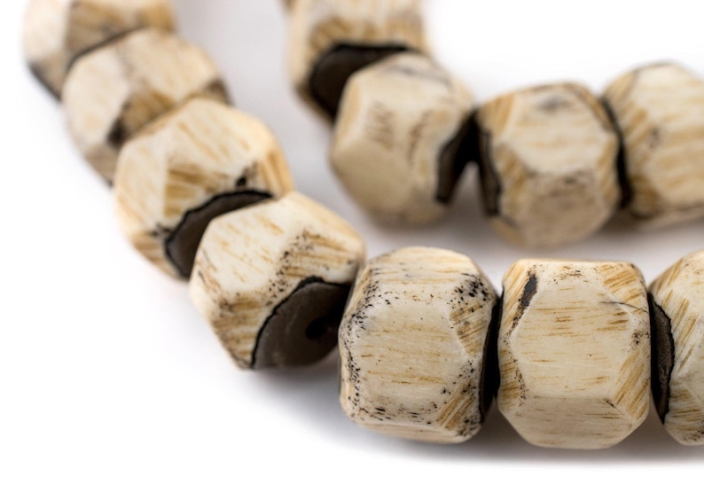 May include: A close-up of a strand of beige and brown wooden beads. The beads are faceted and have a rough, natural texture.