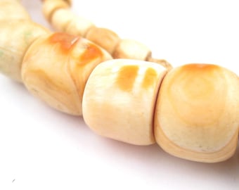 Op de afbeelding: Een close-up van een ketting gemaakt van natuurlijke ivoor kralen. De kralen zijn crèmekleurig met hints van bruin en geel. De kralen zijn glad en gepolijst.