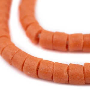 Op de afbeelding: Een close-up van een streng oranje keramische kralen. De kralen zijn rond en hebben een licht getextureerd oppervlak.