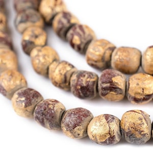 May include: Close-up of three strands of beads. The beads are a mix of burgundy and gold, with a textured, aged appearance. The beads are square-shaped and strung together, creating a necklace or bracelet.
