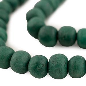 May include: Close-up of a strand of dark green beads. The beads are round with a slightly textured surface. The beads are strung together, forming a curved line against a white background. The beads are approximately 1 cm in diameter.