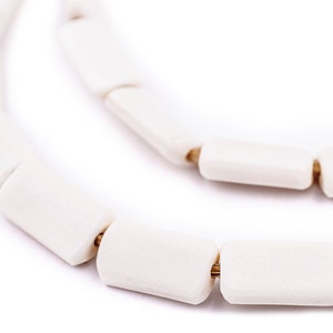 May include: A white ceramic necklace with gold accents. The necklace is made of cylindrical beads that are strung together with a gold wire.