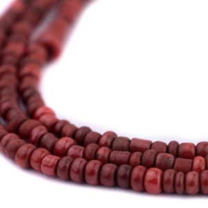 Könnte beinhalten: Nahaufnahme von drei Strängen rotbrauner Holzperlen. Die Perlen sind zylindrisch und rechteckig, mit Farb- und Formvariationen. Der Hintergrund ist schlicht weiß und hebt die Textur und Farbe der Perlen hervor.