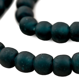 May include: Close-up of a strand of dark teal beads. The beads are round with a slightly flattened shape and a matte finish. The beads are strung together, creating a necklace or bracelet.