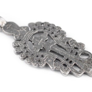 May include: A silver-toned pendant in the shape of a cross with intricate details and a loop at the top for hanging.