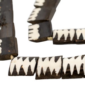 Puede incluir: Primer plano de un collar hecho de cuentas de hueso negro y blanco. Las cuentas están talladas con un patrón geométrico y están enhebradas con un cordón delgado.