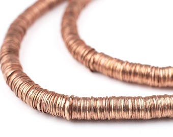 Puede incluir: Primer plano de un collar de color cobre hecho de cuentas redondas planas apiladas. Las cuentas están dispuestas en un patrón circular, creando un aspecto único y texturizado.