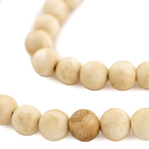 May include: A strand of off-white beads with one brown bead in the centre.