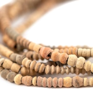 Könnte beinhalten: Nahaufnahme von mehreren Strängen beige-brauner Perlen. Die Perlen variieren in Form und Größe, einige erscheinen zylindrisch, andere runder. Die Perlen sind aufgefädelt und erzeugen einen geschichteten Effekt vor weißem Hintergrund.