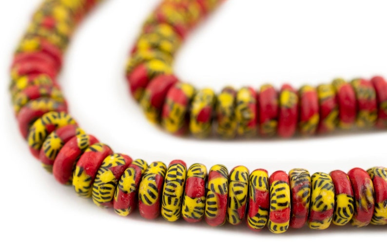 May include: A strand of red and yellow glass beads with a black geometric pattern. The beads are round and have a slightly flattened shape.