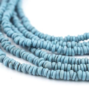Op de afbeelding: Close-up van verschillende strengen lichtblauwe, schijfvormige kralen. De kralen zijn aan elkaar geregen, waardoor een gelaagd effect ontstaat. De kralen hebben een licht ruwe textuur en een matte afwerking.
