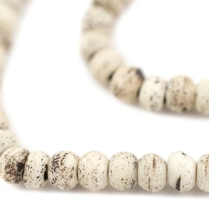 May include: A strand of white and brown speckled beads, strung together in a circular pattern.