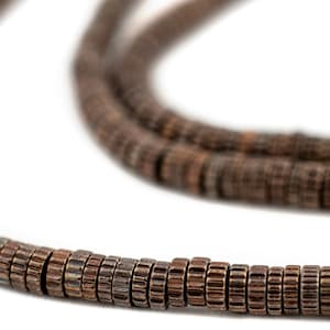May include: A close-up of a brown beaded necklace made of small, round, textured beads. The beads are strung together to form a long, continuous strand.