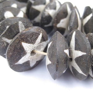 Può includere: Una collana di perline in ceramica nera con disegni a forma di stella bianca. Le perline sono rotonde e hanno una forma leggermente irregolare.