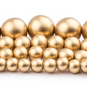 K&ouml;nnte beinhalten: Eine Sammlung goldfarbener Holzperlen in verschiedenen Gr&ouml;&szlig;en. Die Perlen sind in einem versetzten Muster angeordnet, wodurch ein visueller Effekt einer kaskadierenden Wasserfall entsteht.