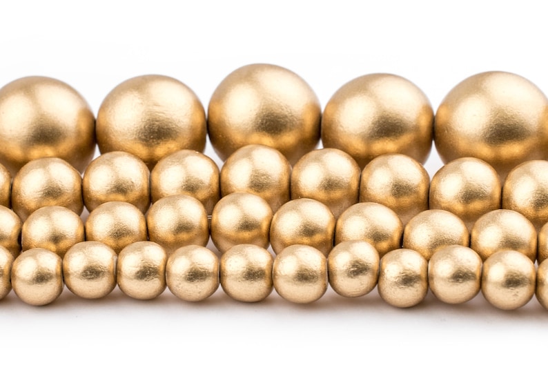 K&ouml;nnte beinhalten: Eine Sammlung goldfarbener Holzperlen in verschiedenen Gr&ouml;&szlig;en. Die Perlen sind in einem versetzten Muster angeordnet, wodurch ein visueller Effekt einer kaskadierenden Wasserfall entsteht.