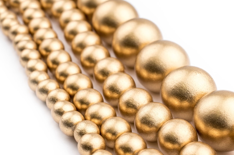 K&ouml;nnte beinhalten: Eine Reihe goldfarbener Holzperlen in verschiedenen Gr&ouml;&szlig;en. Die Perlen sind rund und haben eine glatte, matte Oberfl&auml;che.