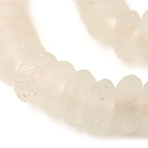 May include: Close-up of a strand of off-white, frosted glass beads. The beads are irregularly shaped, with a slightly flattened, oval design. The surface of the beads has a textured, matte finish, and the color is a soft, creamy white.