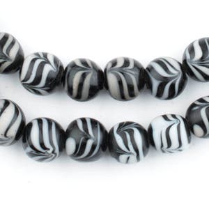 Könnte beinhalten: Eine Kette aus schwarzen und weißen Glasperlen mit einem Wirbelmuster. Die Perlen sind rund und haben eine glänzende Oberfläche.