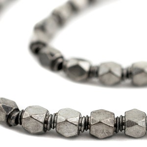 May include: Close-up of a silver-toned necklace with geometric, faceted beads. The beads are strung together with a dark metal wire, creating a textured and detailed accessory. The necklace is displayed against a white background.