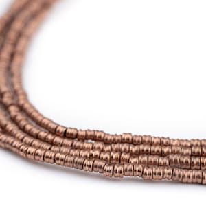 May include: A close-up of a strand of copper-colored beads. The beads are small and round, and they are arranged in a tight, even pattern.