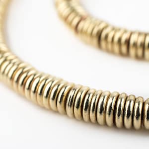 Puede incluir: Un collar de oro hecho de pequeñas cuentas redondas y unidas. Las cuentas son lisas y brillantes, y el collar es un diseño simple y elegante.