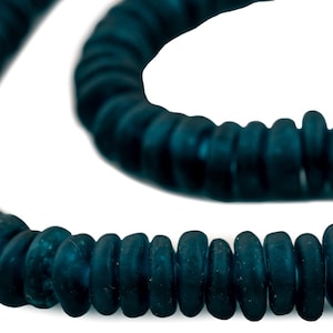 May include: A necklace of dark teal beads, each with a rounded, flattened shape. The beads are strung together, forming a curved line against a white background. The beads have a matte finish.
