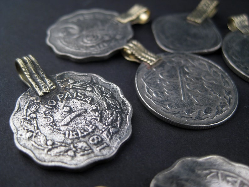 May include: A collection of six silver coins with gold loops, each featuring a different design and the inscription "10 Paisa".