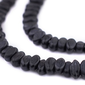 May include: Close-up of two strands of black, irregular-shaped beads. The beads have a smooth, glossy finish and are strung together, creating a necklace or bracelet. The background is plain white, highlighting the dark beads.