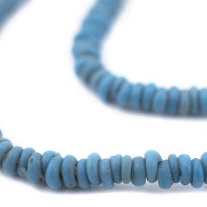 Pode incluir: Um fio de contas de vidro azul, enfiadas para formar um colar. As contas são pequenas e redondas, com uma forma ligeiramente irregular.