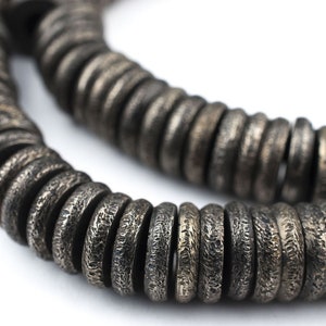 May include: A strand of dark gray metal beads with a textured surface. The beads are round and have a slightly raised edge.