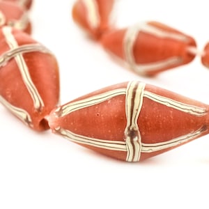 Può includere: Una collana di perline di vetro rosso e bianco con un motivo geometrico. Le perline sono infilate su un filo sottile.