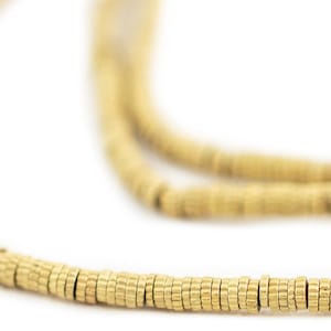 Peut inclure: Gros plan sur un collier doré avec un motif de perles. Le collier est composé de petites perles cylindriques enfilées ensemble. Les perles ont un éclat métallique et sont disposées en motif linéaire. Le fond est blanc.