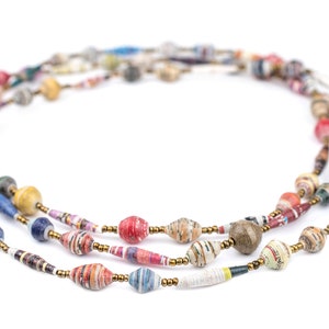 May include: A multi-strand necklace made of colorful paper beads. The beads are made of rolled up paper and are in various colors, including red, blue, green, yellow, and brown. The necklace is strung on a gold cord.