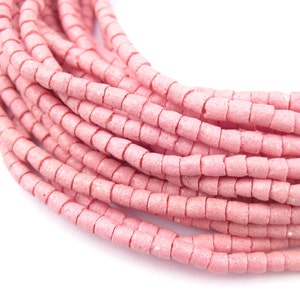Op de afbeelding: Close-up van verschillende strengen roze, vierkante kralen. De kralen hebben een getextureerde, matte afwerking en zijn aan elkaar geregen, waardoor een opgerold patroon ontstaat. De achtergrond is wit, waardoor de kleur en textuur van de kralen worden benadrukt.