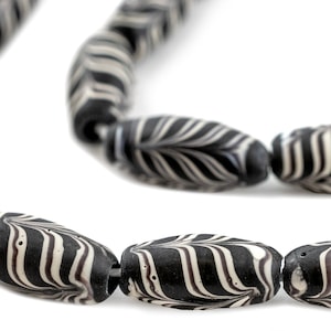 Puede incluir: Primer plano de un collar hecho de cuentas ovaladas de rayas blancas y negras. Las cuentas están hechas de un material liso y pulido y tienen un acabado ligeramente brillante.