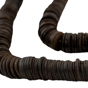 Może przedstawiać: Długi sznur ciemnobrązowych, okrągłych, płaskich koralików, nawleczonych na sznurek, tworząc naszyjnik. Korale są ułożone jeden na drugim, tworząc gruby, linowy wygląd.