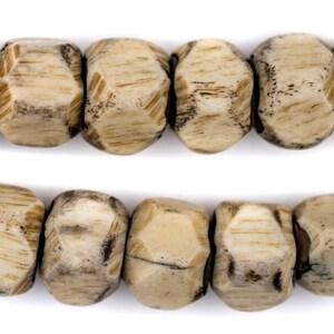 May include: A strand of beige and brown wooden beads with a faceted, geometric shape. The beads are strung together on a white background.