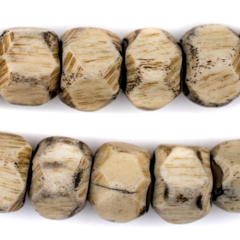 May include: A strand of beige and brown wooden beads with a faceted, geometric shape. The beads are strung together on a white background.