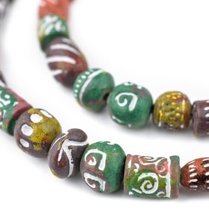 Pode incluir: Close-up de um fio de contas coloridas e artesanais. As contas têm várias formas, incluindo redondas e cilíndricas, e apresentam padrões intrincados em branco, verde, castanho e amarelo. As contas são enfiadas, criando um acessório decorativo.