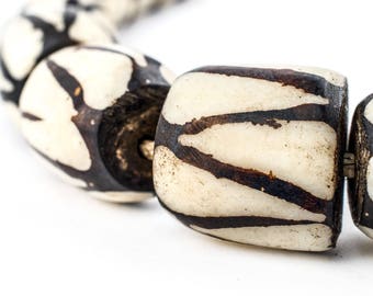 May include: Close-up of a necklace made of white and brown patterned beads. The beads are round and have a smooth, polished finish.