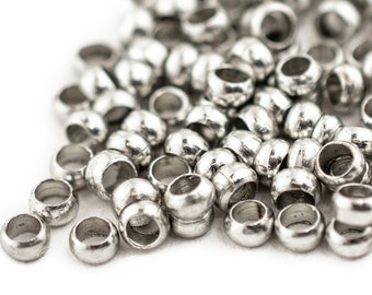 May include: A pile of silver metal beads, some are scattered on a white surface.